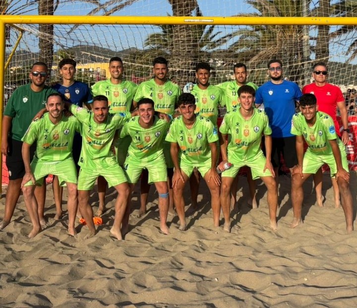 Beach soccer team in neon green jerseys posing in front of a net on a sandy beach.