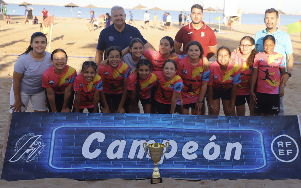 Youth girls' soccer team and coaches posing on the beach with a 'Campeón' banner and trophy in front