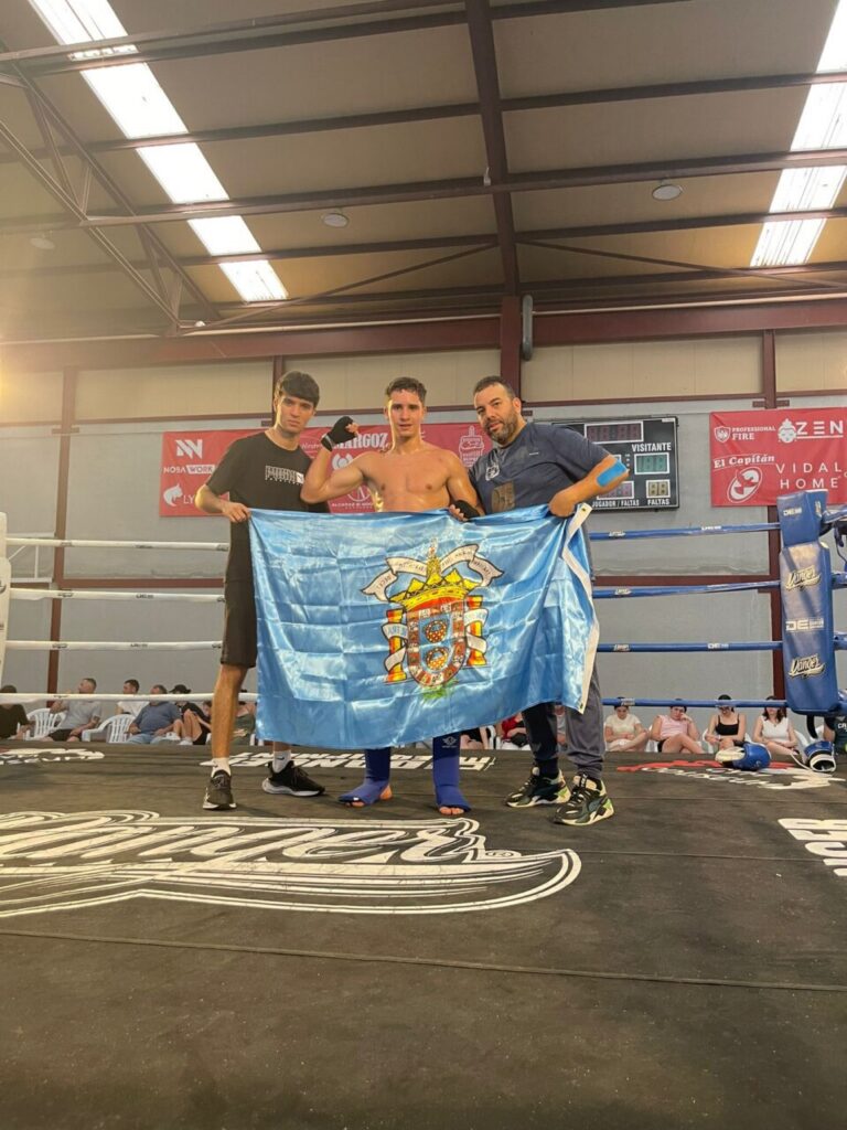 Boxer posing with two companions in a ring, holding a blue Portugal flag with crest visible among the ropes.
