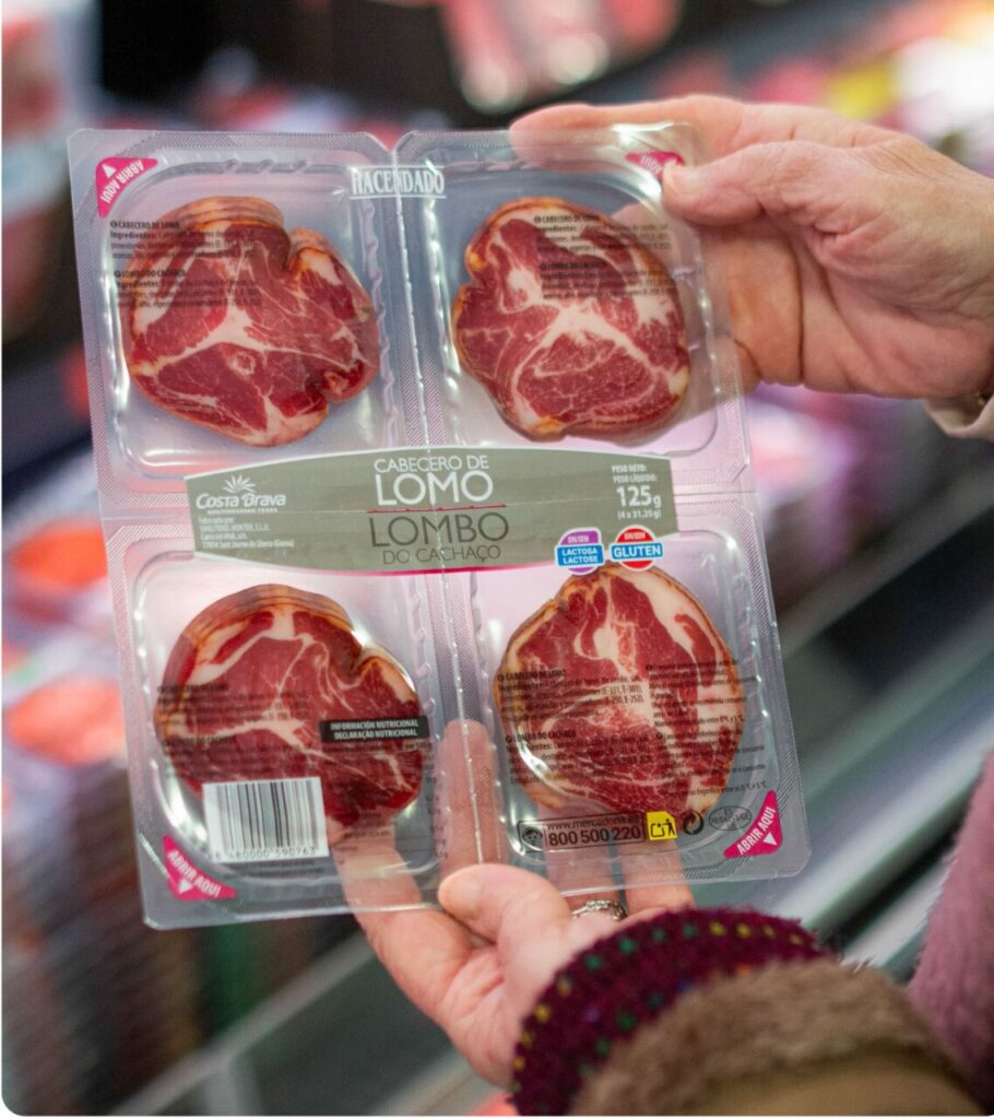 Four raw beef medallions in a plastic tray labeled 'LOMO' being shown in a shopper's hands at a supermarket.