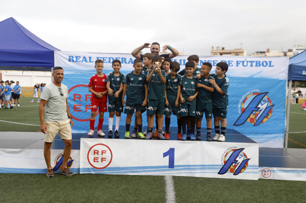 Youth soccer team on a winner's podium with coach, posing in teal uniforms after a match.