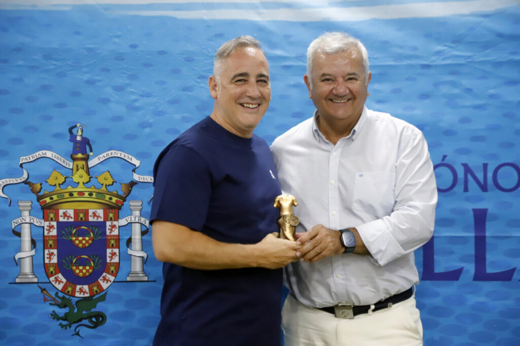 Dos hombres sonrientes sosteniendo un trofeo en un evento deportivo