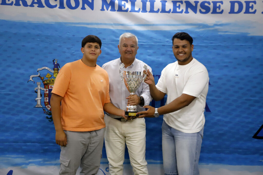 Tres personas sosteniendo un trofeo en un evento de fútbol en Melilla
