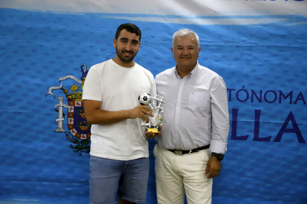 Dos hombres sosteniendo un trofeo en un evento deportivo de fútbol
