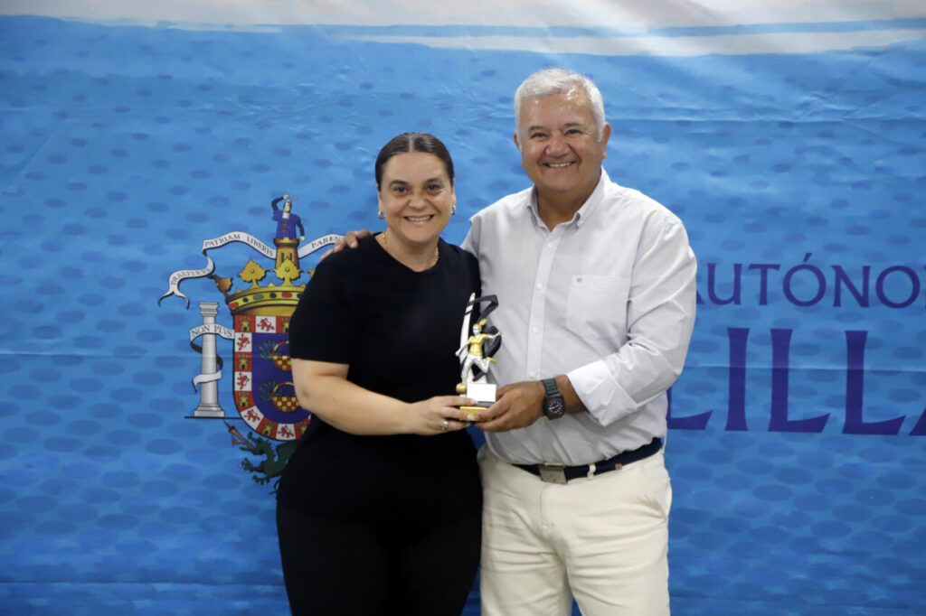 Dos personas sonrientes sosteniendo un trofeo en un evento deportivo.