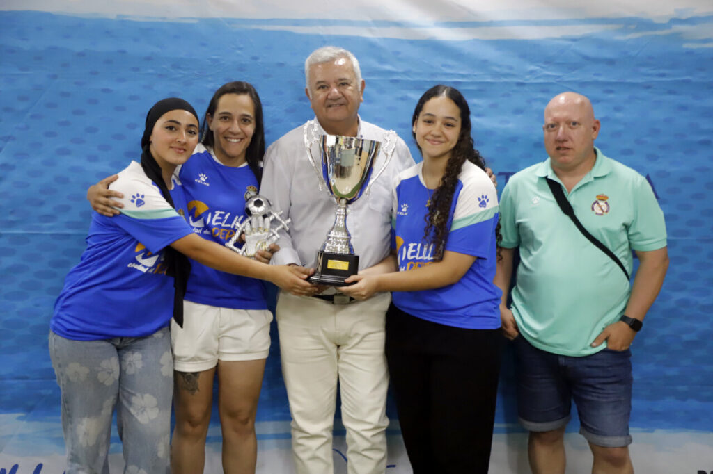 Group of five celebrating with a trophy, posing for a photo against a blue backdrop of a sports banner