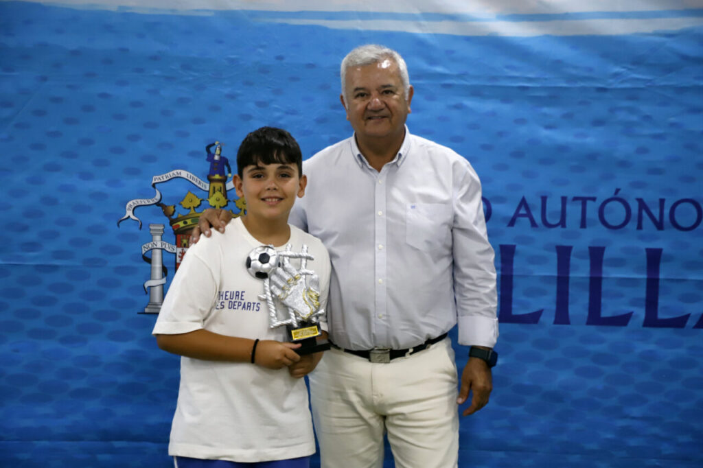 Niño sosteniendo un trofeo de fútbol junto a un adulto en un evento deportivo