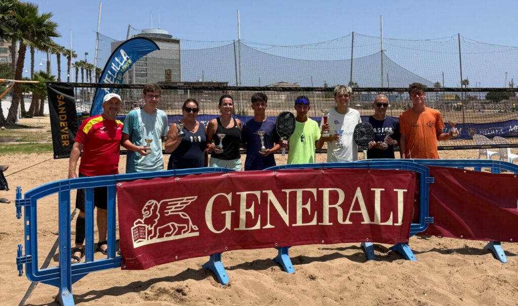 Group of people on a sandy paddle tennis court posing with trophies in front of a Generali banner and net backdrop, smiling at the camera.
