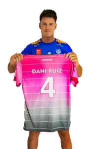 Man in a blue jersey holds up a pink gradient sports jersey showing the name 'DANI-RUIZ' and the number 4 in white.