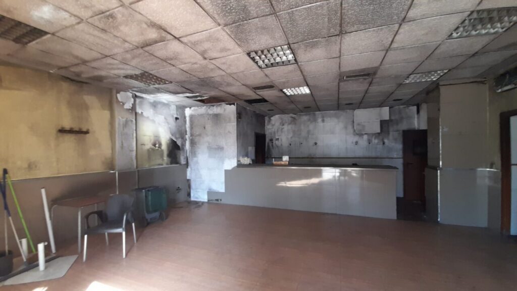 Abandoned reception area with a long counter, peeling walls, and a sagging, soot-stained ceiling.