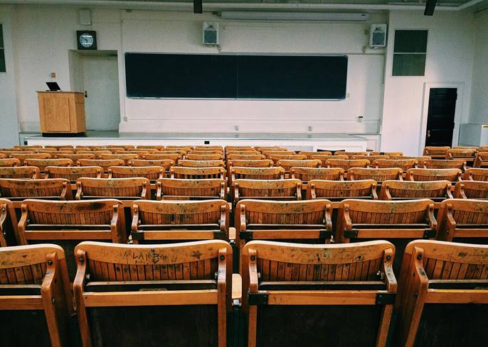 Aula vacía con asientos de madera y pizarra en la pared.