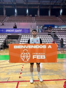 Jugador de baloncesto sosteniendo un cartel de bienvenida a la Primera FEB