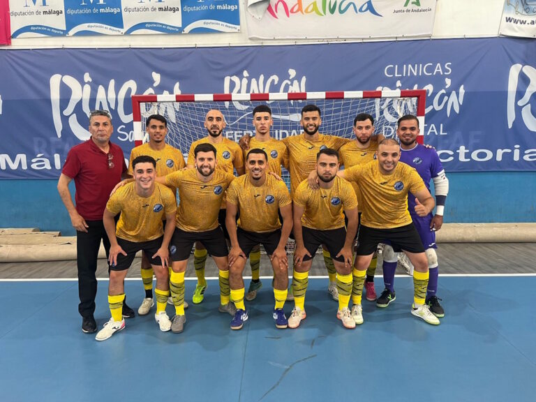 Futsal team in yellow jerseys posing in front of a goal inside an indoor court.