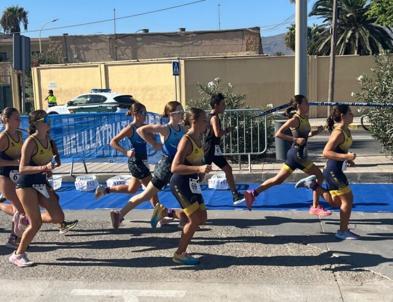 Group of young female runners in yellow and blue race kits sprint along a city street.