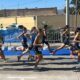 Group of young female runners in yellow and blue race kits sprint along a city street.