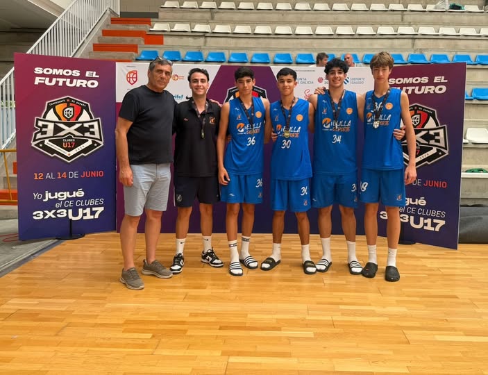 Six young basketball players in blue uniforms pose with two coaches on a gym floor, banners behind them read 'Somos el Futuro' and show a club logo.