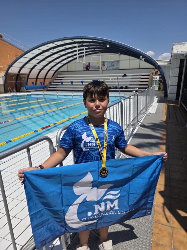 Niño del Club Natación Melilla con medalla y bandera en la piscina