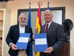 Dos hombres sosteniendo documentos en un acto de firma de convenio