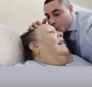 Hombre besando la frente de una mujer mayor en una cama