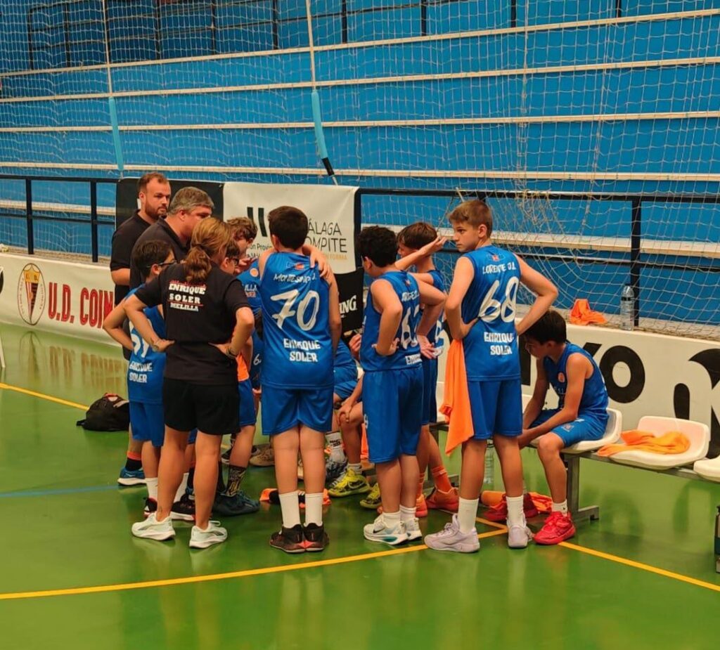 Youth basketball team in blue uniforms huddles with coach on an indoor court.