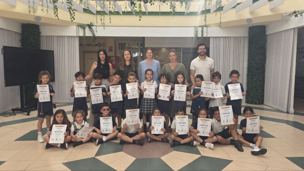 Group of smiling elementary students holding certificates with their teachers in a school atrium. 🏫✨