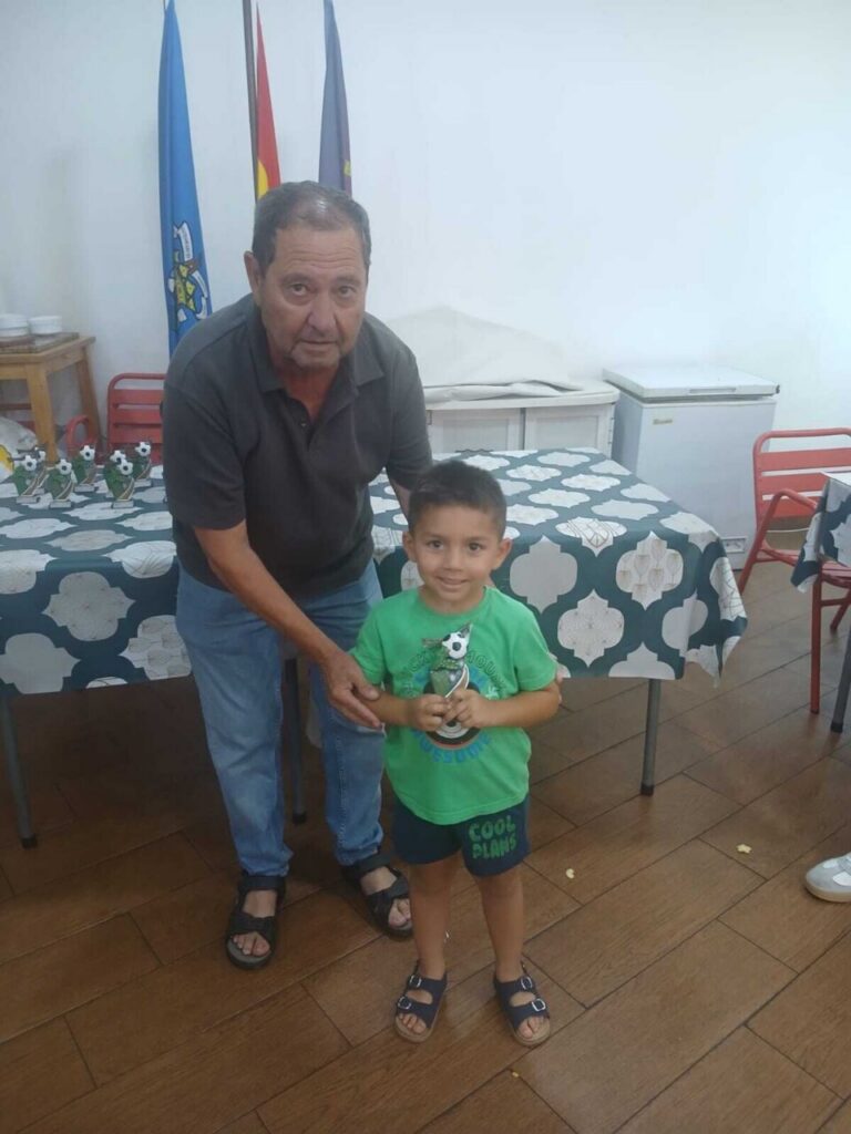 Un niño sonriente sostiene un trofeo junto a un adulto en un evento escolar.
