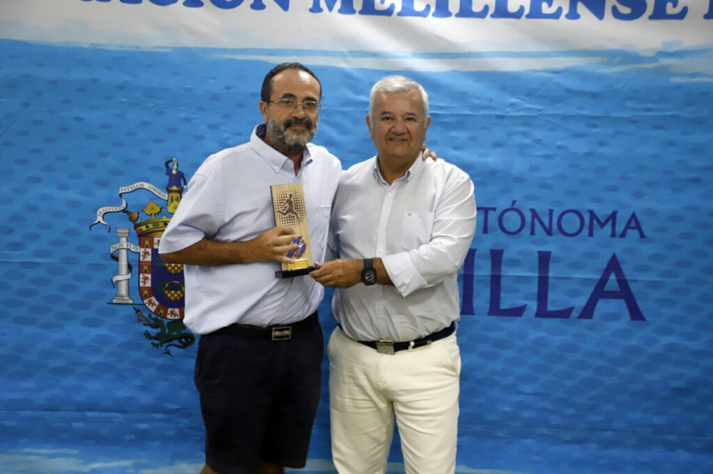 Dos hombres sosteniendo un trofeo en un evento de fútbol en Melilla.