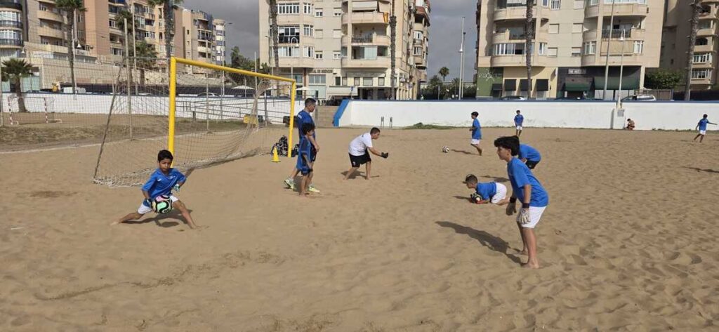 Niños entrenando fútbol en la playa con un arco de fútbol