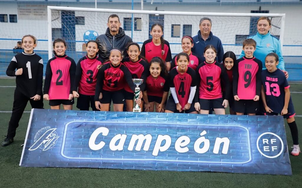 Equipo alevín femenino posando con trofeo en campo de fútbol