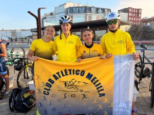 Cuatro triatletas del Club Atlético Melilla sosteniendo una bandera del club