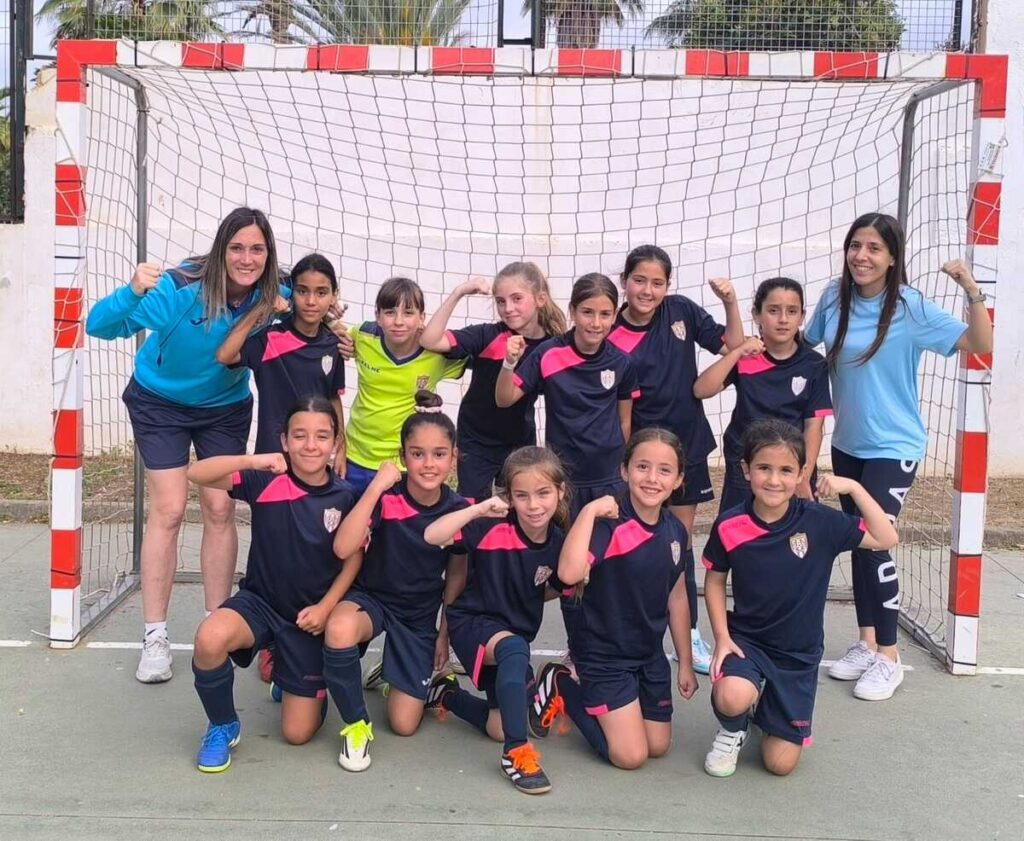 Equipo femenino de fútbol sala Benjamín posando con fuerza en la cancha