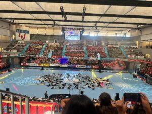 Vista del pabellón lleno durante un evento deportivo con actuaciones en el suelo.