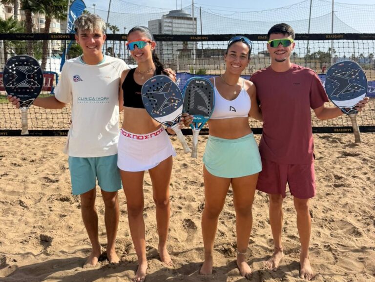 Cuatro jugadores sosteniendo palas de pádel en la playa