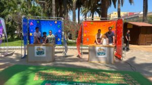 Two colorful letter-themed game booths with families playing an alphabet challenge outdoors in a sunny park setting.