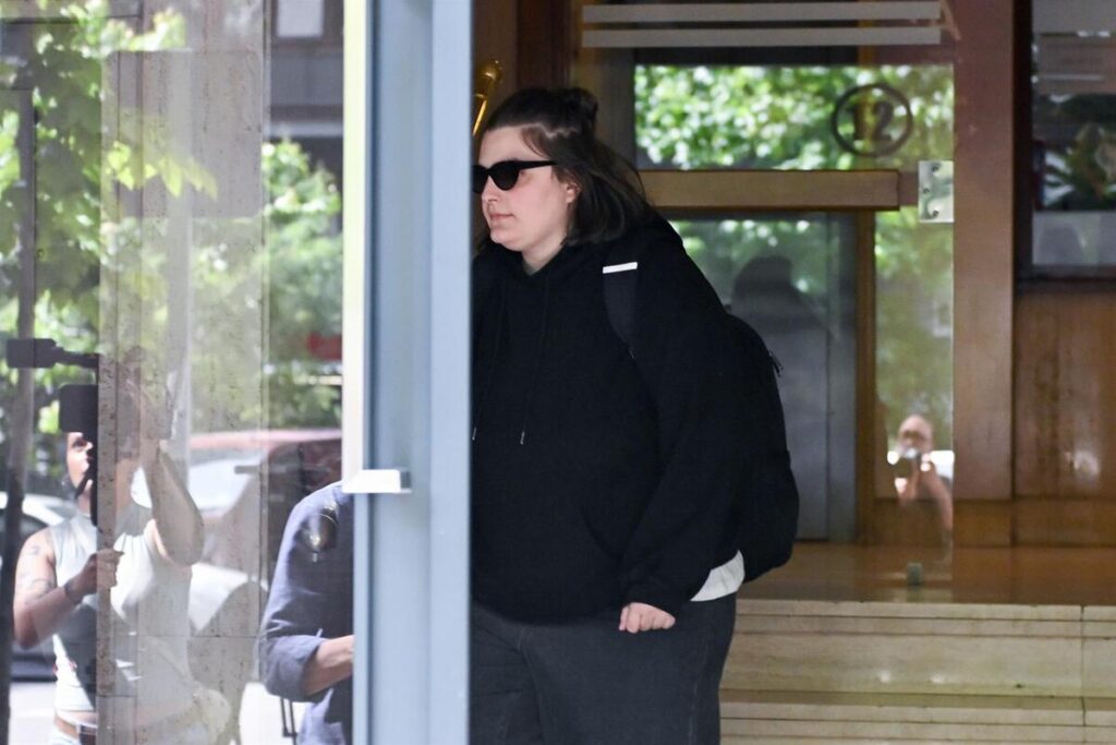 Mujer con gafas de sol y sudadera negra saliendo de un edificio