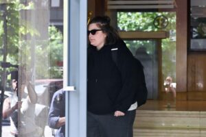 Mujer con gafas de sol y sudadera negra saliendo de un edificio