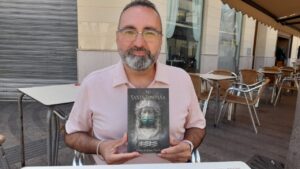 Jesús Andújar Martín sosteniendo su libro Mi Santa Compaña en una mesa