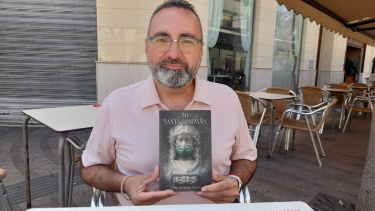Jesús Andújar Martín sosteniendo su libro Mi Santa Compaña en una mesa
