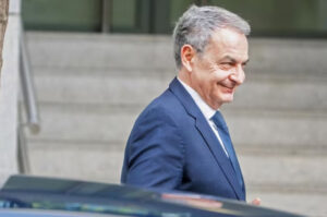 José Luis Rodríguez Zapatero sonriendo mientras sale de un edificio.