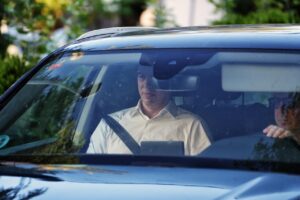 Man driving a blue car, wearing a seatbelt and looking at a tablet on the dashboard.