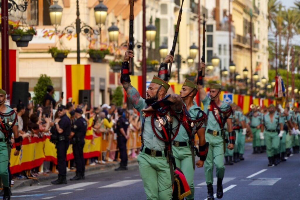 Desfile militar en Melilla con soldados marchando y público animando.