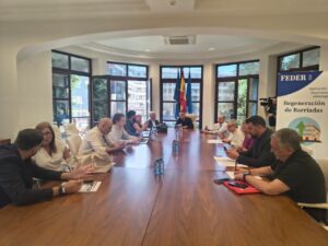 Group of people seated around a long conference table in a bright room; flags and a FEDER banner are visible in the background.