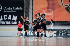 Grupo de jugadoras de fútbol sala en uniforme negro celebrando en la cancha junto a la portería central.
