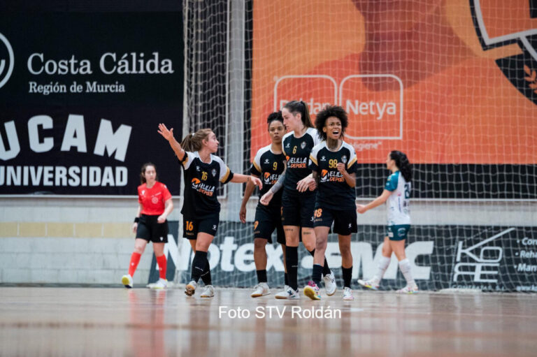 Grupo de jugadoras de fútbol sala en uniforme negro celebrando en la cancha junto a la portería central.