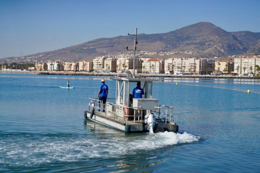 Embarcación anticontaminación navegando en la playa con fondo de edificios