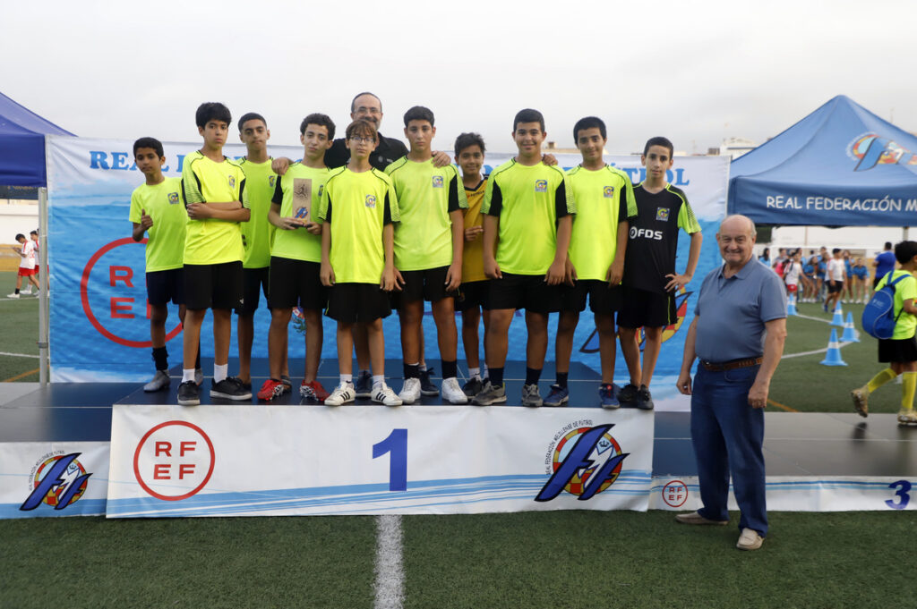 Youth soccer team posing on a first-place podium with trophies, wearing neon green jerseys, flanked by coaches and event banners behind them.