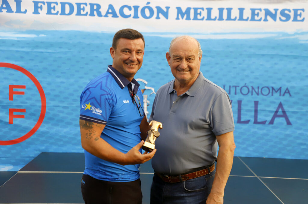 Dos hombres sonrientes sosteniendo un trofeo en un evento deportivo