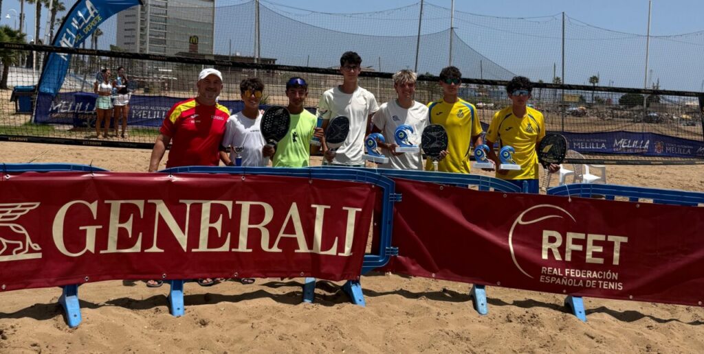 Group of young players and a coach posing with trophies on a sandy beach tennis court, behind red Generali and RFET banners.