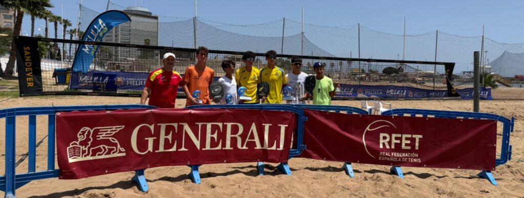 Group of seven people (six players and a coach) posing behind a red Generali banner on a sandy beach tennis court, with RFET banner nearby.