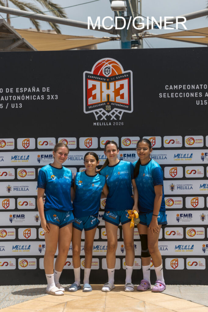 Four female basketball players in matching blue uniforms pose together in front of a 3x3 Spain championship backdrop in Melilla.